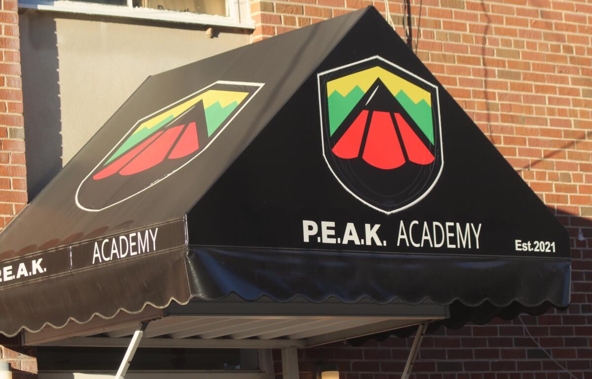 The awning outside PEAK Academy is black with a logo that includes the red tip of a pencil with yellow and green trim.