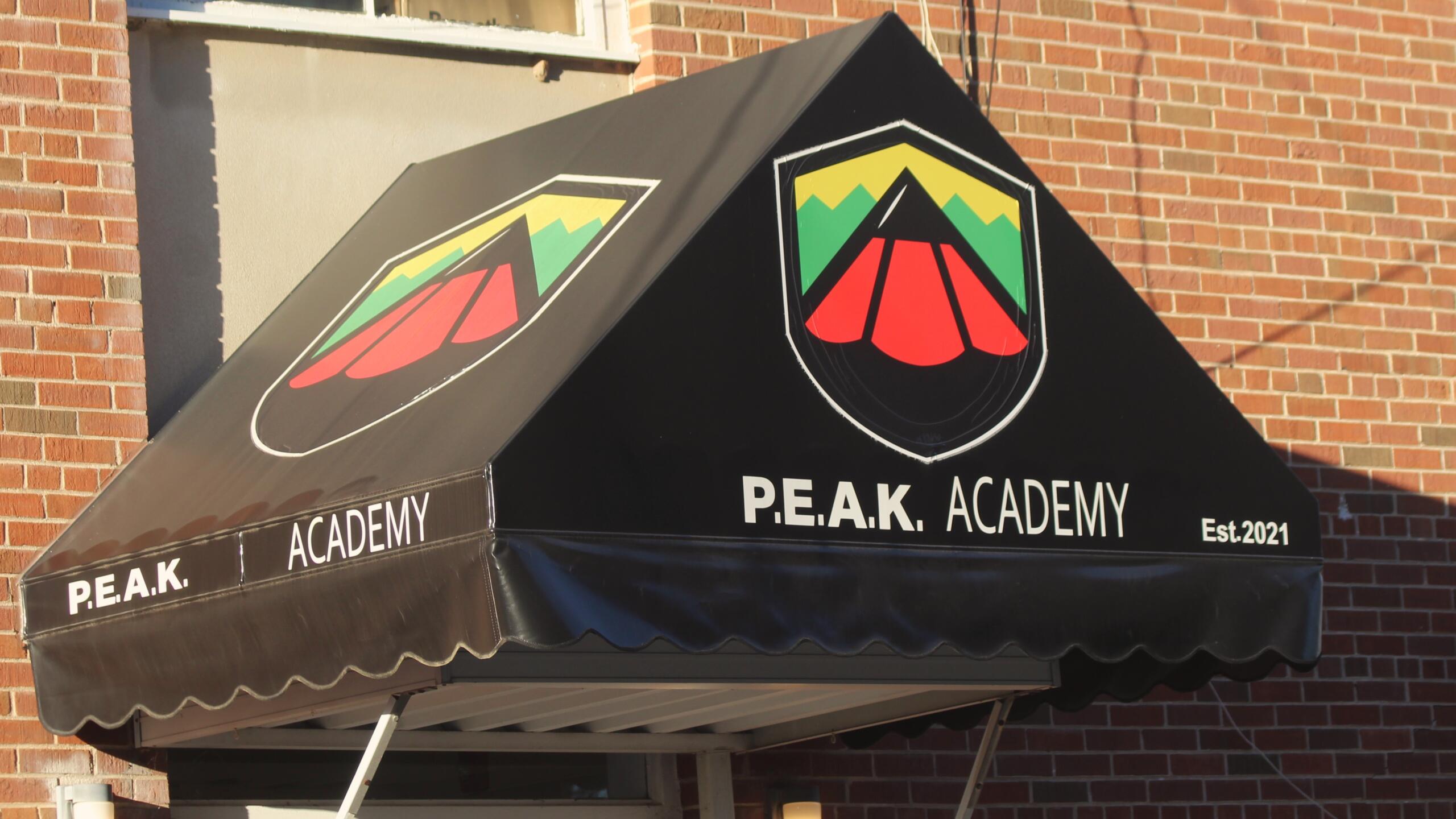 The awning outside PEAK Academy is black with a logo that includes the red tip of a pencil with yellow and green trim.