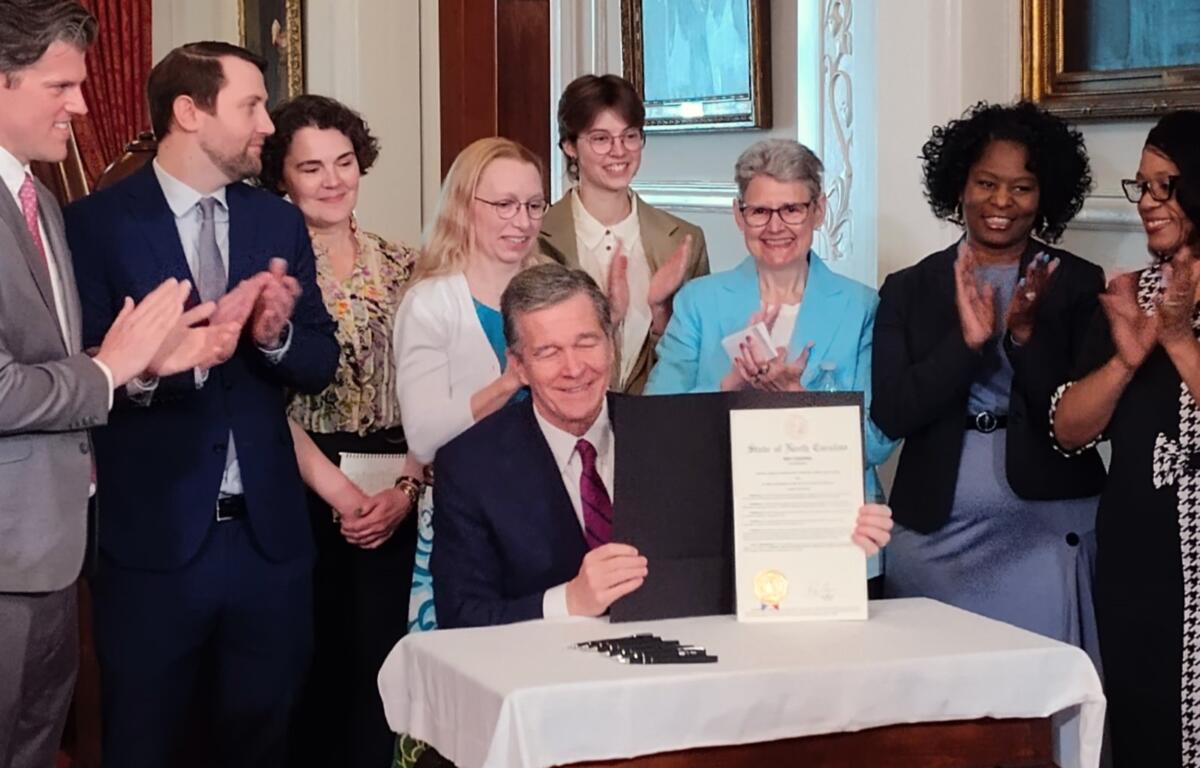 North Carolina Gov. Roy Cooper signs a proclamation celebrating assisters who enroll people in health care coverage, surrounded by member of the NC Navigator Consortium and the Care Share Health Alliance, April 16, 2024.
