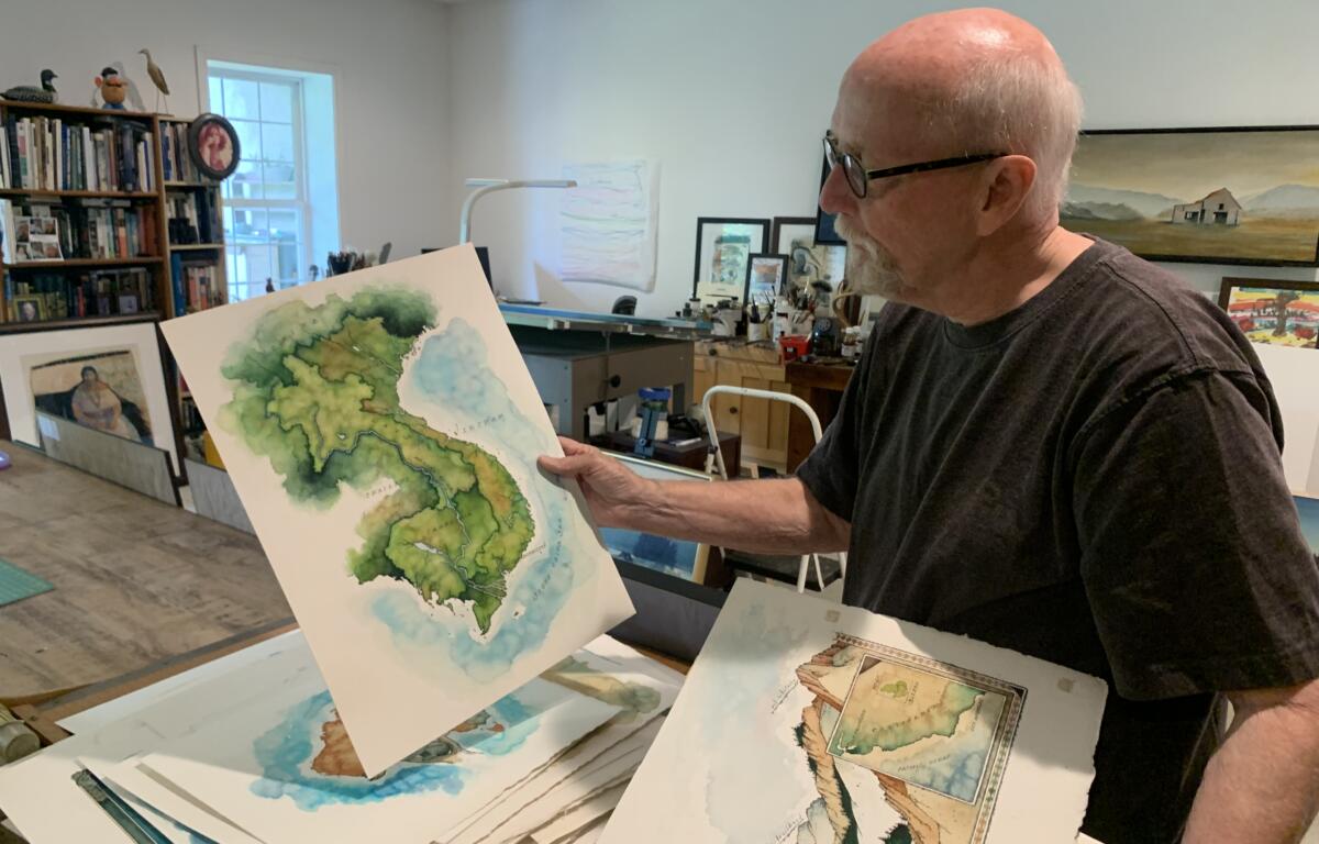 Michael Francis Reagan shows off one of his works, a map of southeast Asia, at his home studio. Considered the "Last Mapmaker" for his hand-made methods, his works will be shown this summer at Grovewood Gallery.