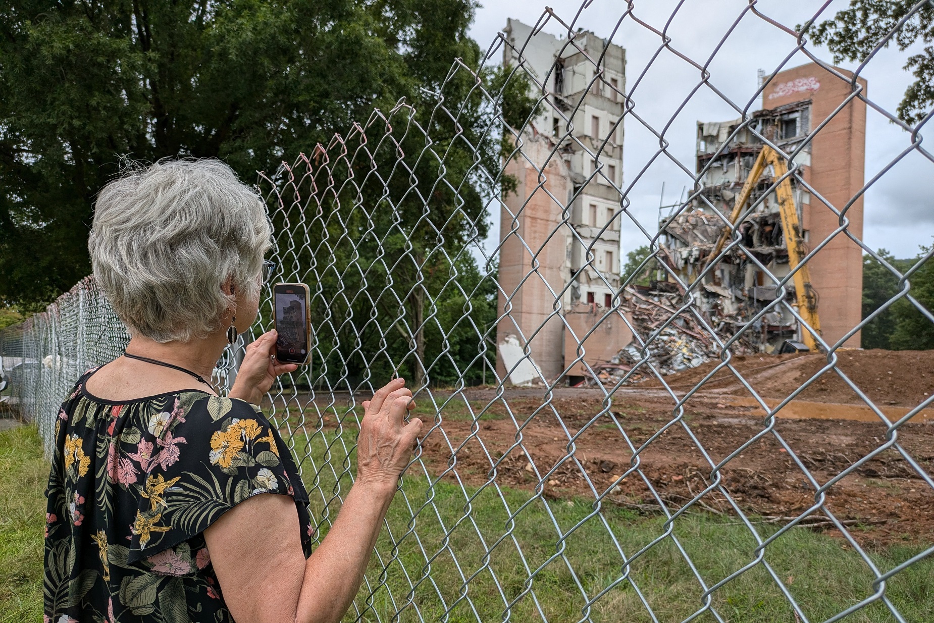 Lisa Schwartz of Candler takes a cell phone video as a large section of the former Haynes Tower came tumbling down on Thursday, July 25, 2024, at A-B Tech's campus in Enka.