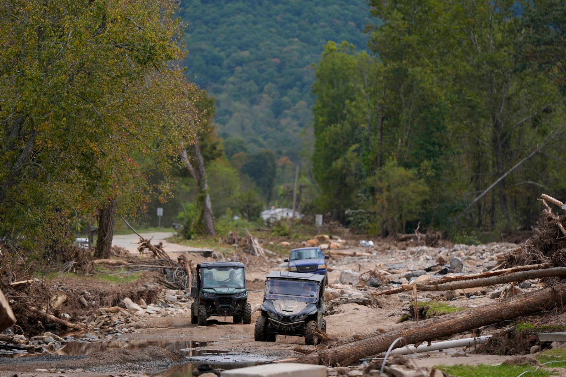 Vehicles roll along on a washed up road in the aftermath of Hurricane Helene, Thursday, Oct. 3, 2024, in Pensacola, N.C. (AP Photo/Mike Stewart)
