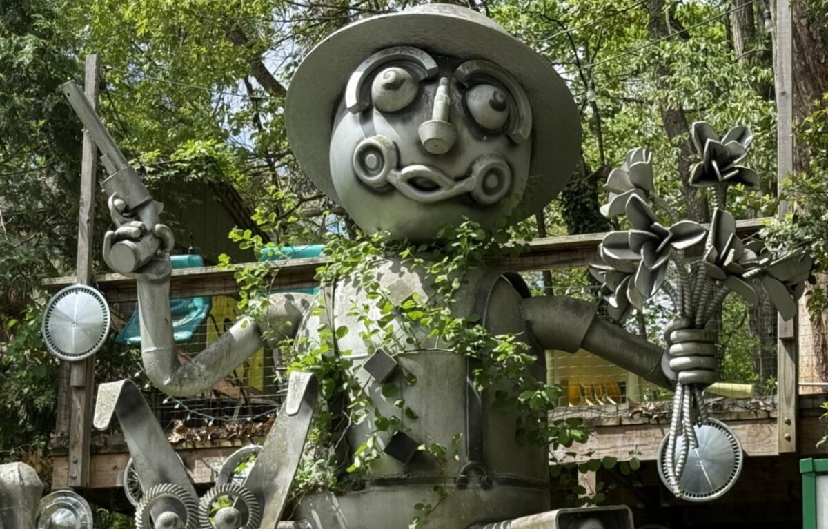 A large metal sculpture depicting a man riding a wheeled pig or dog while carrying a six-shooter and a bouquet of flowers stands at the entrance to the Burton Street community's Peace Gardens & Market.