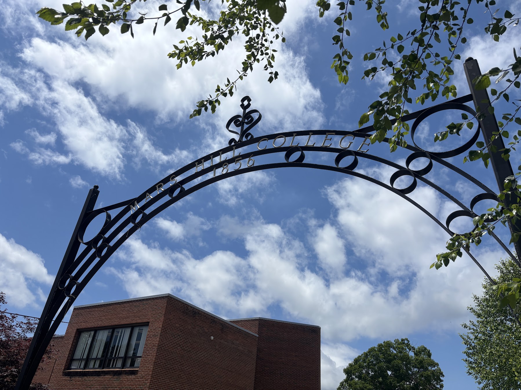 A metal sign for Mars Hill College stands against a blue sky.