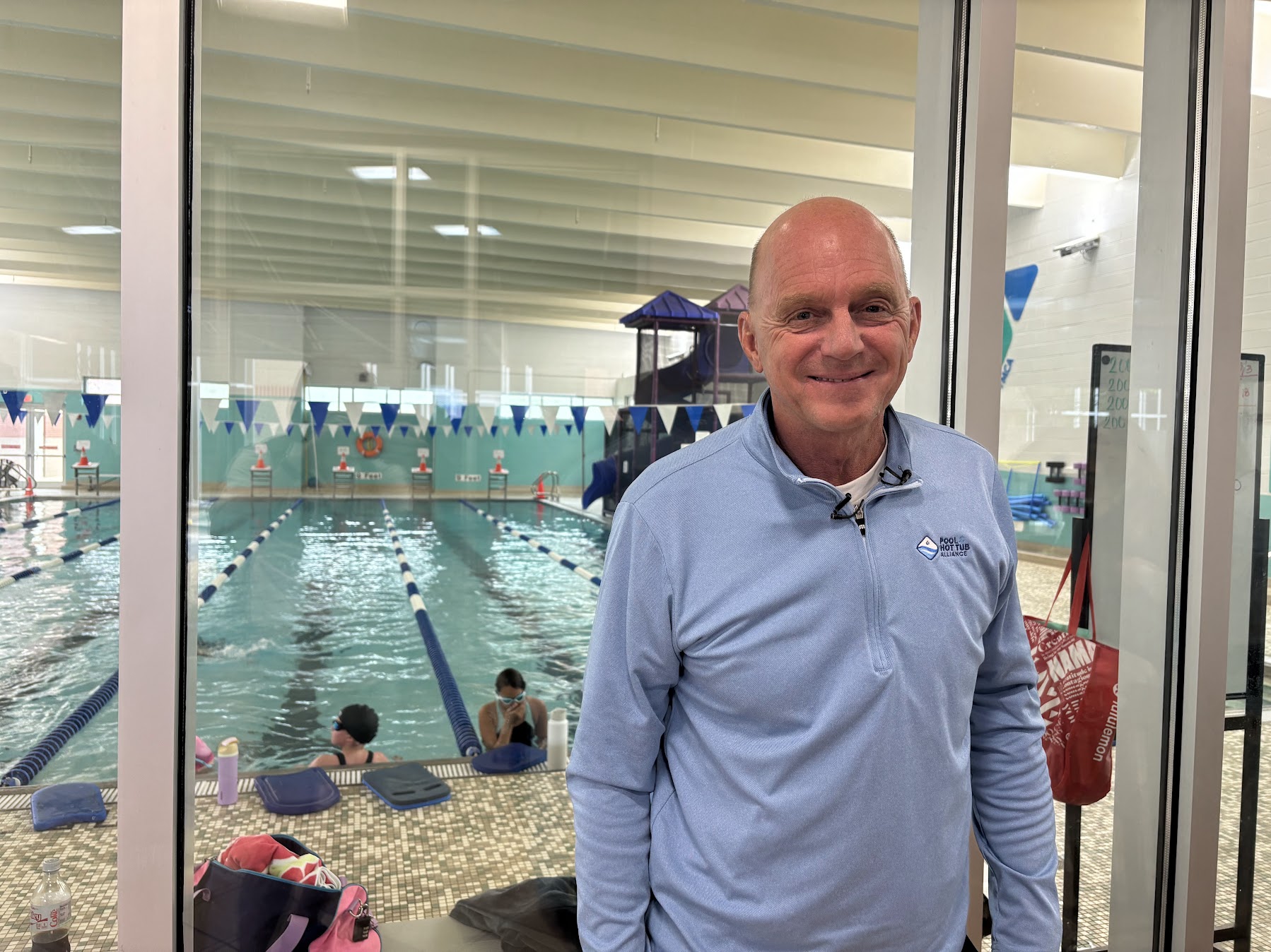 Olympian Rowdy Gaines stands in front of glass with a pool behind him.