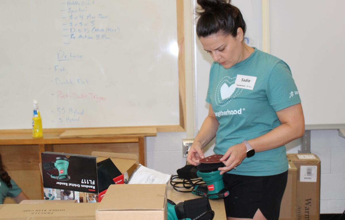 Sadie Simpson puts sandpaper on a sander as volunteers get a bookcase ready to be painted.