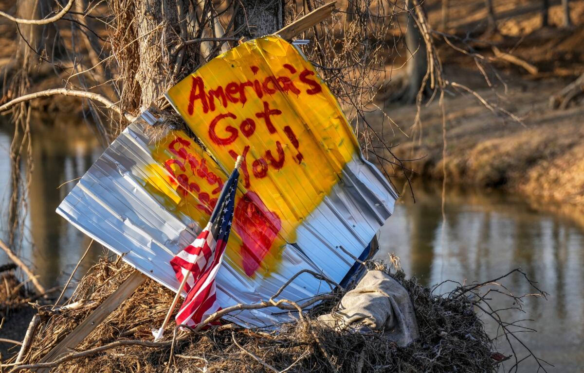 An American flag stands next to a sign written on housing debris along the Swannanoa River, Wednesday, Feb. 5, 2025, in Swannanoa, N.C. Swannanoa was one of several communities in western North Carolina that was severely affected by Hurricane Helene. (AP Photo/Kathy Kmonicek)