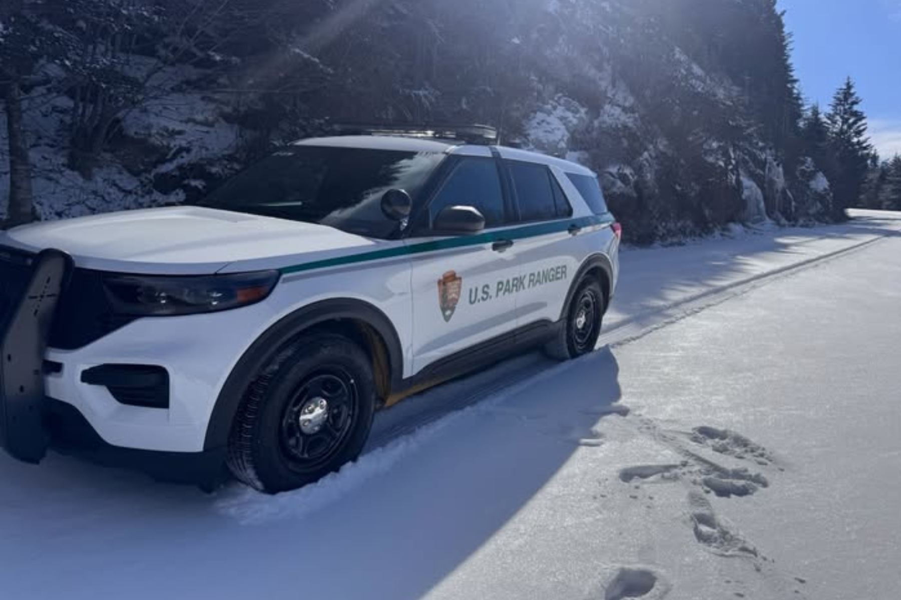 Law enforcement vehicle near a snow-covered mountainside.