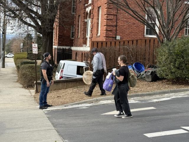An Asheville animal services vehicle and two city forensic vehicles are seen in the parking lot of an apartment complex off Merrimon Avenue Tuesday afternoon, where a man wearing a vest marked “POLICE” escorted individuals from the vehicles.