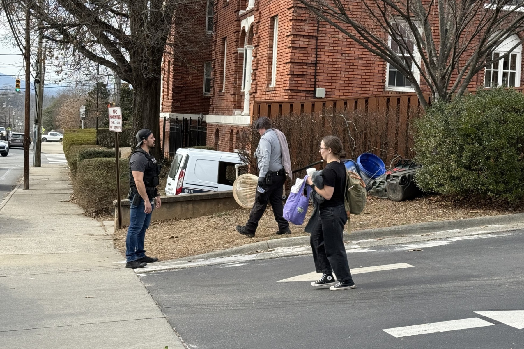 An Asheville animal services vehicle and two city forensic vehicles are seen in the parking lot of an apartment complex off Merrimon Avenue Tuesday afternoon, where a man wearing a vest marked “POLICE” escorted individuals from the vehicles.