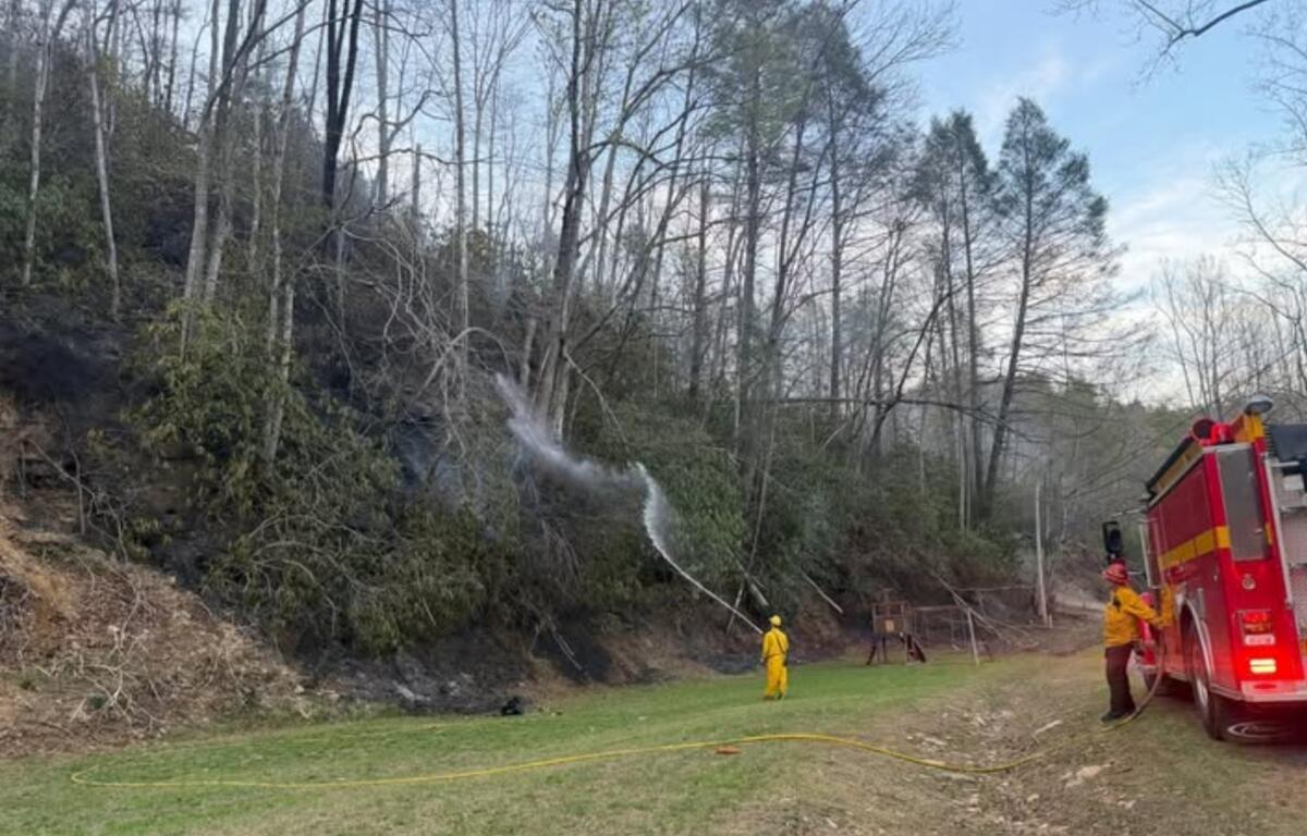 A firefighter sprays water on the Jumping Branch Fire near a road. (Photo credit: U.S. Forest Service/Allyson Pokrzywinski)