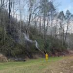 A firefighter sprays water on the Jumping Branch Fire near a road. (Photo credit: U.S. Forest Service/Allyson Pokrzywinski)