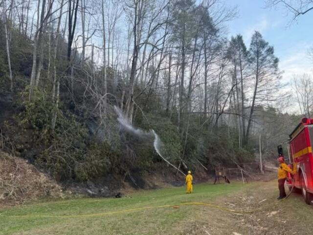 A firefighter sprays water on the Jumping Branch Fire near a road. (Photo credit: U.S. Forest Service/Allyson Pokrzywinski)