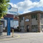 Public parking sign and stone office building at 52 Coxe Avenue, with a tree-lined foreground and a blue sky.