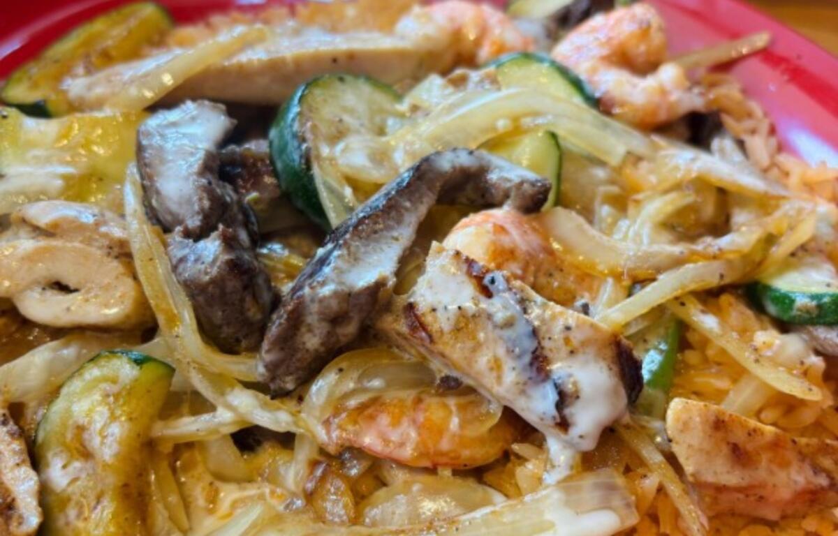 Creamy pasta dish with shrimp, sliced chicken, onions, zucchini, and other vegetables on a pink plate.