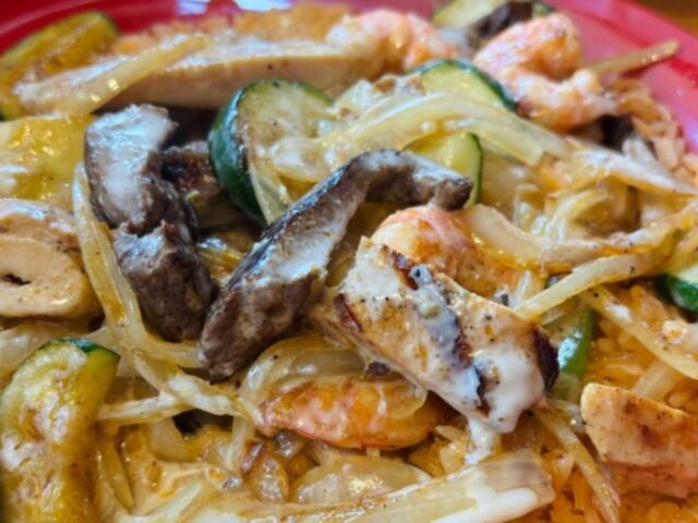 Creamy pasta dish with shrimp, sliced chicken, onions, zucchini, and other vegetables on a pink plate.