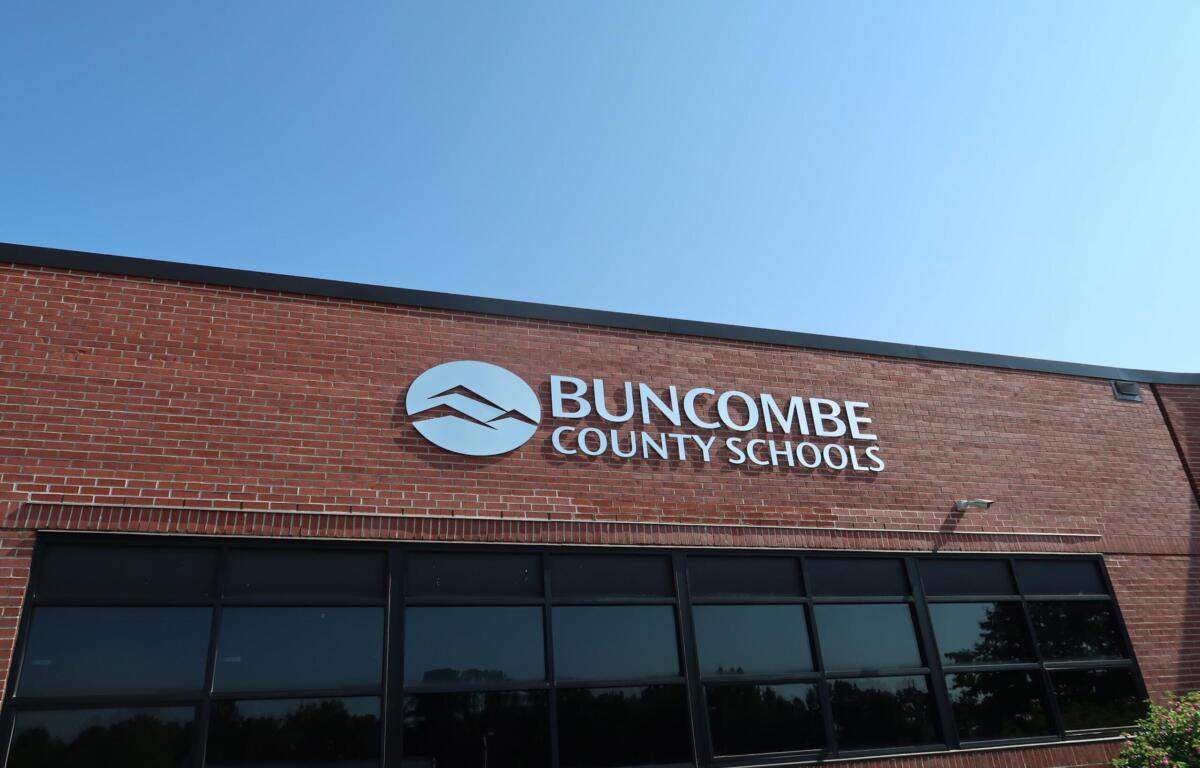 Exterior view of Buncombe County Schools building with a circular logo and white lettering on red brick under a clear blue sky