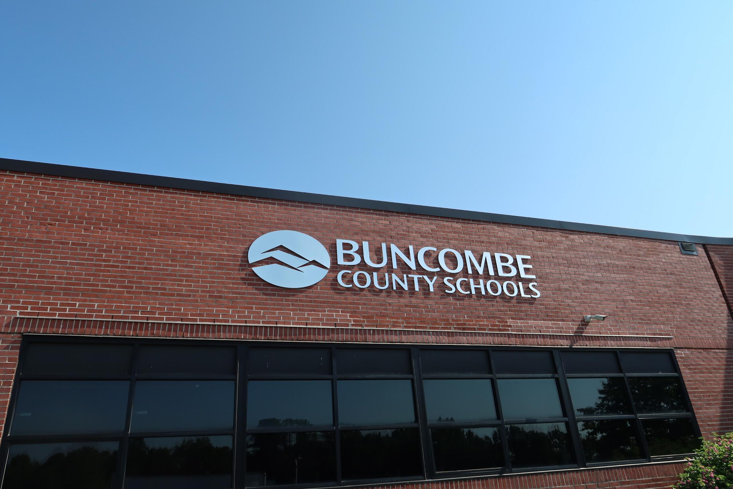 Exterior view of Buncombe County Schools building with a circular logo and white lettering on red brick under a clear blue sky