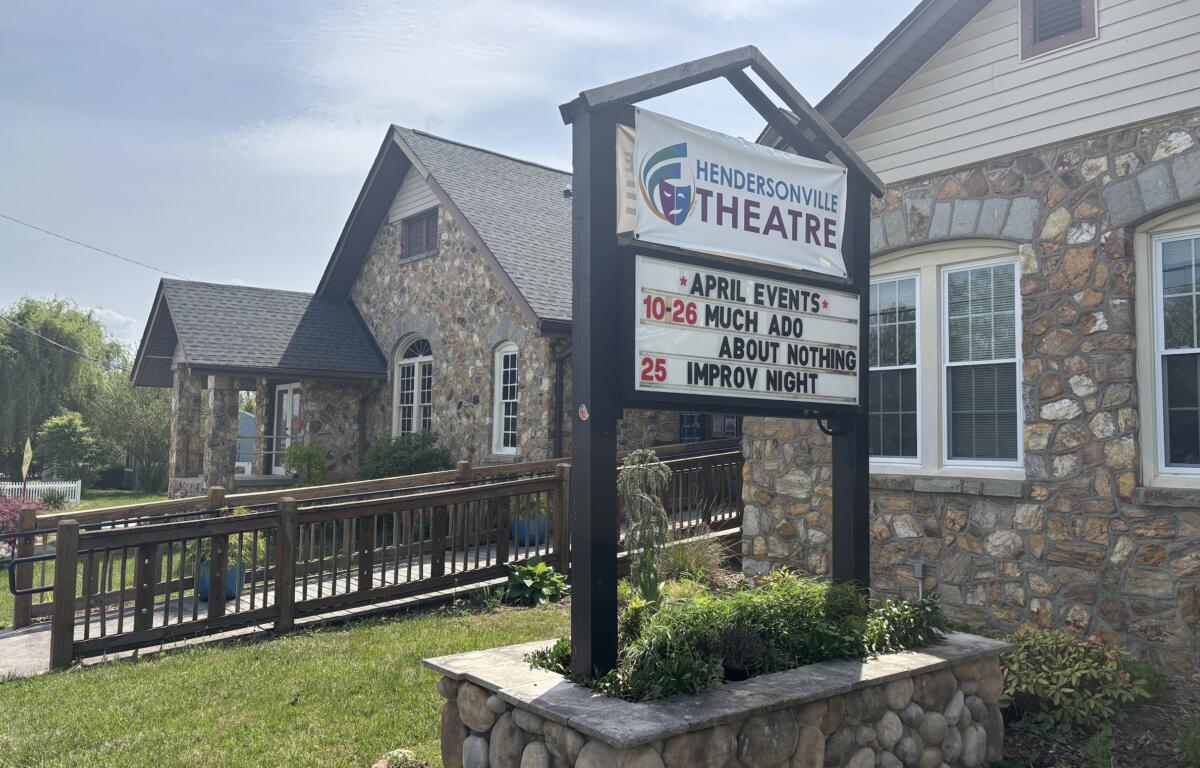 Hendersonville Theatre sign on a stone building with an events board listing April shows and dates outdoors under a blue sky