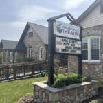 Hendersonville Theatre sign on a stone building with an events board listing April shows and dates outdoors under a blue sky