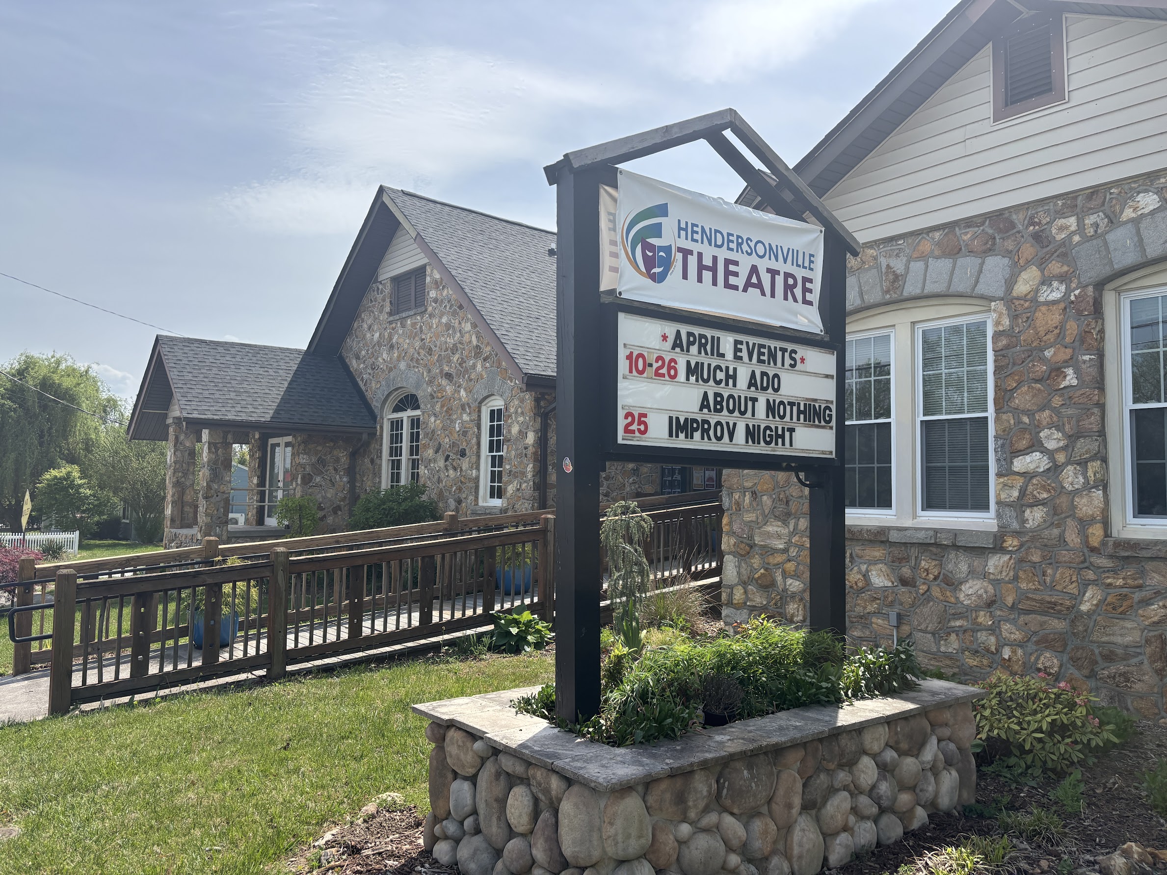 Hendersonville Theatre sign on a stone building with an events board listing April shows and dates outdoors under a blue sky