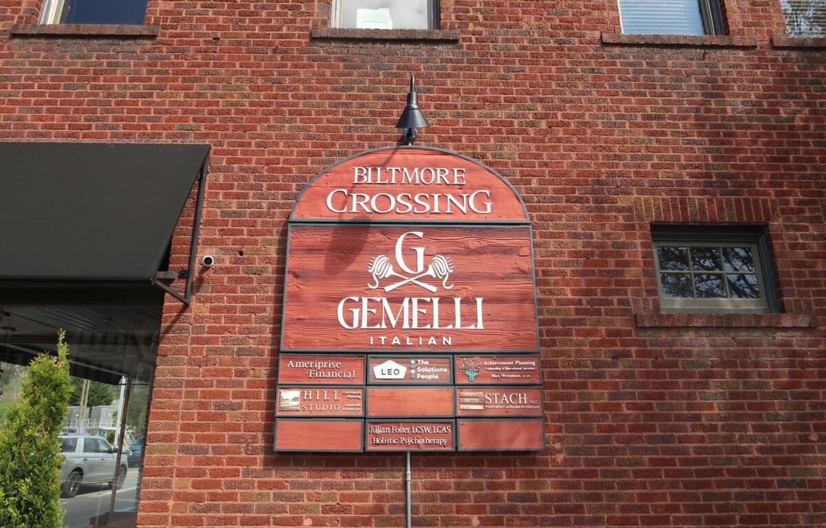 Brick building façade with an arched red sign reading 'Biltmore Crossing Gemelli Italian' and smaller tenant plaques below.