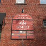 Brick building façade with an arched red sign reading 'Biltmore Crossing Gemelli Italian' and smaller tenant plaques below.