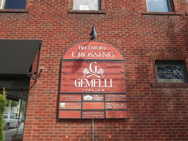 Brick building façade with an arched red sign reading 'Biltmore Crossing Gemelli Italian' and smaller tenant plaques below.