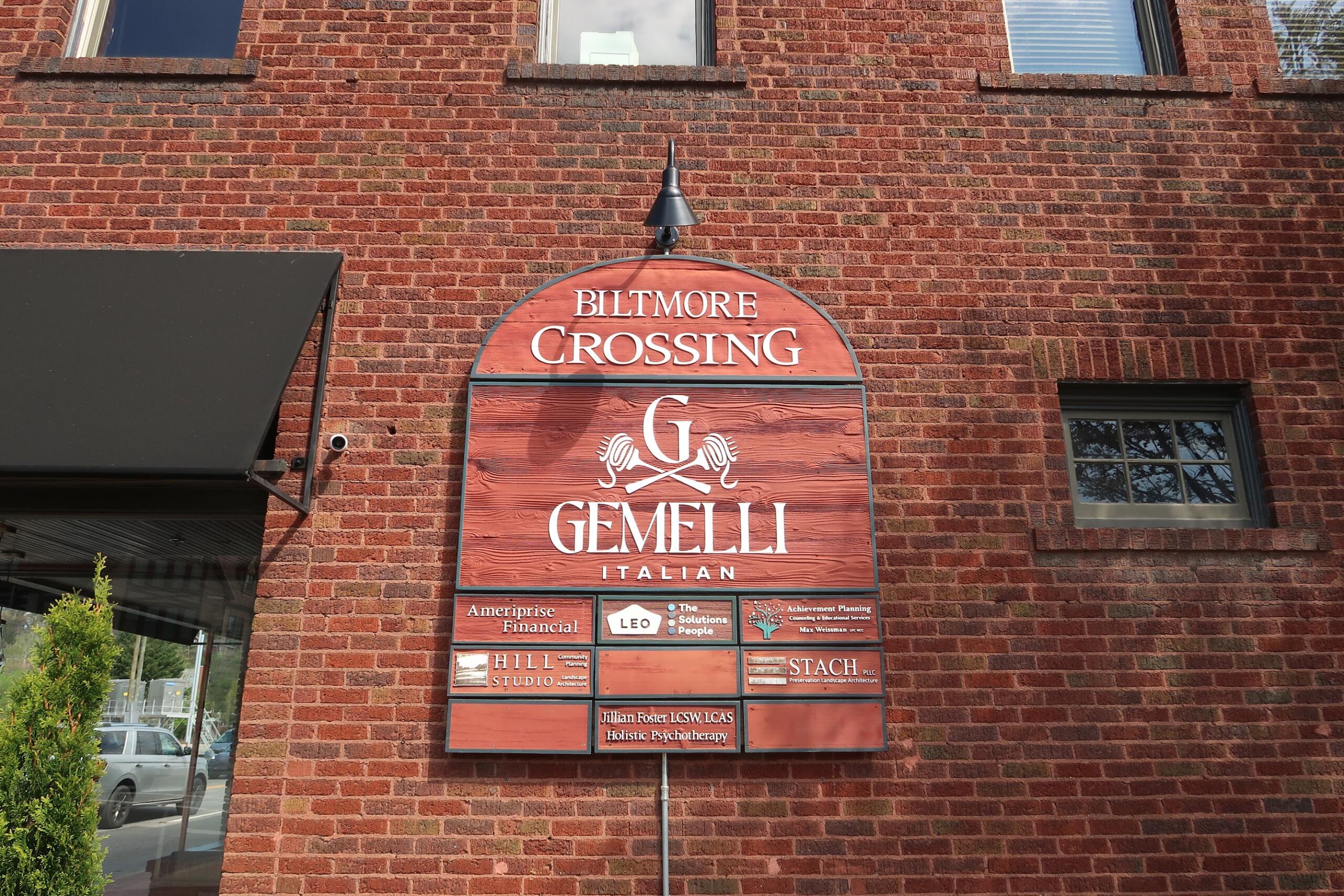 Brick building façade with an arched red sign reading 'Biltmore Crossing Gemelli Italian' and smaller tenant plaques below.