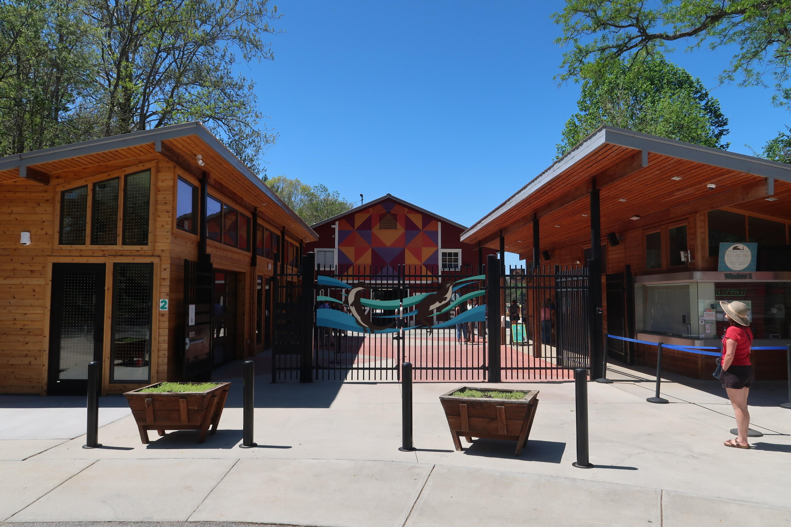Entrance to a park or zoo with wooden buildings on each side and a decorative gate featuring teal and blue waves.