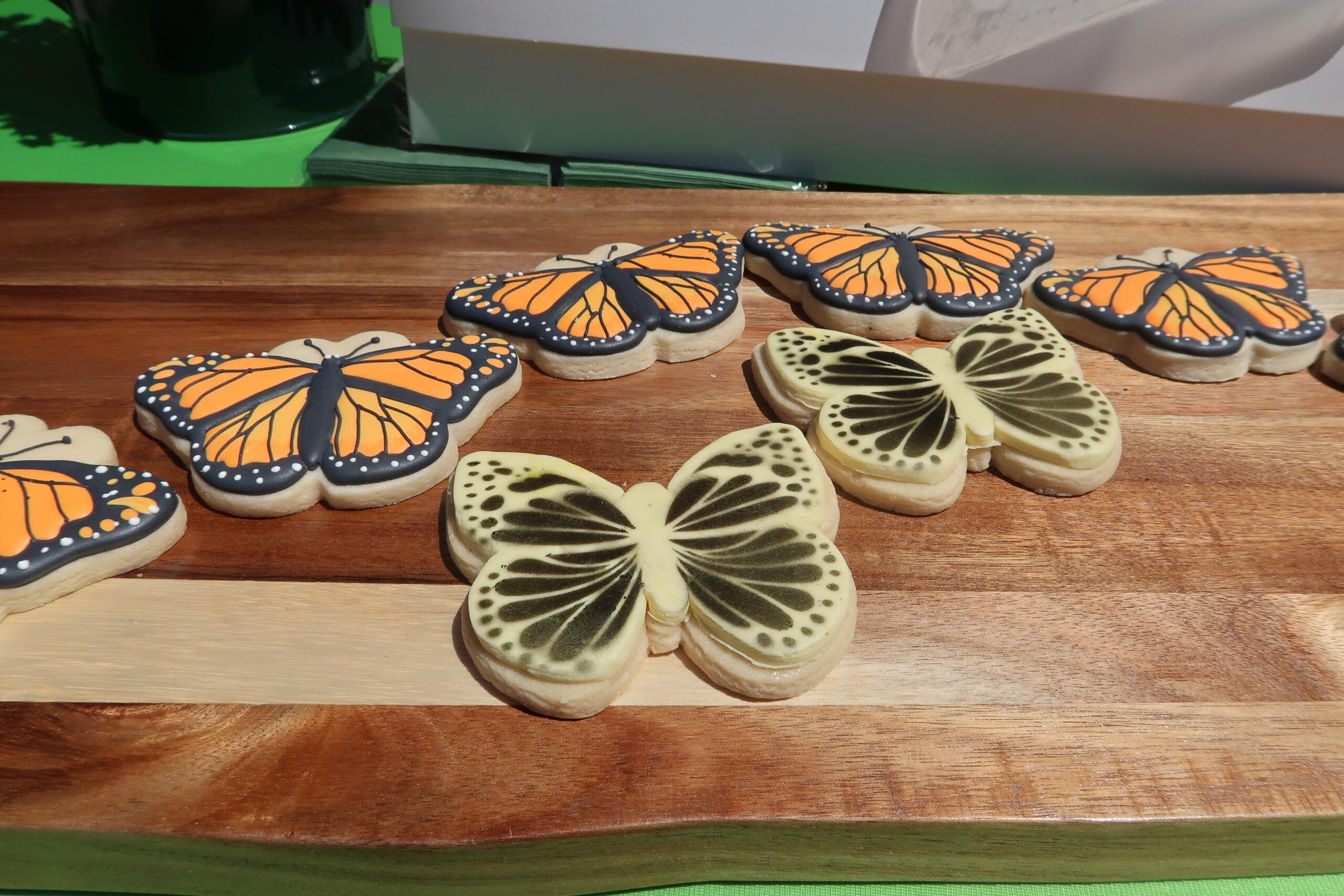 Butterfly-shaped cookies with orange monarch wings outlined in black on a wooden board, arranged in a row with some cream-colored butterflies beside them.