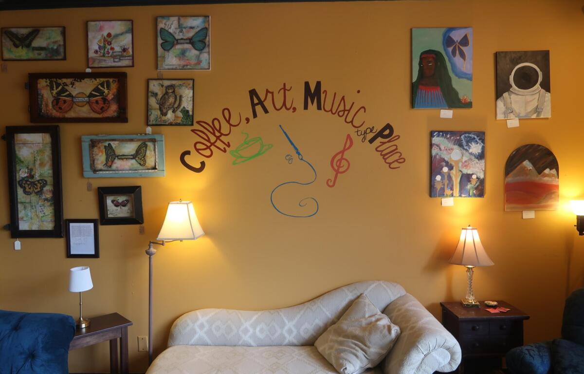 Living room with a gallery wall on a mustard-yellow wall, featuring many framed artworks around a cursive text design, a beige sofa, and two lamps.