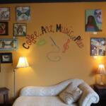 Living room with a gallery wall on a mustard-yellow wall, featuring many framed artworks around a cursive text design, a beige sofa, and two lamps.