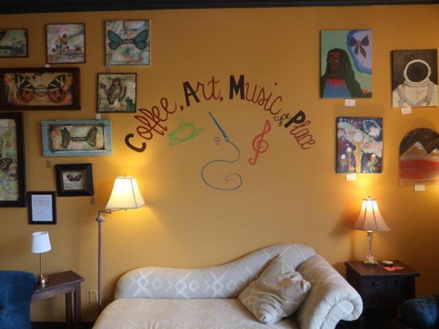 Living room with a gallery wall on a mustard-yellow wall, featuring many framed artworks around a cursive text design, a beige sofa, and two lamps.