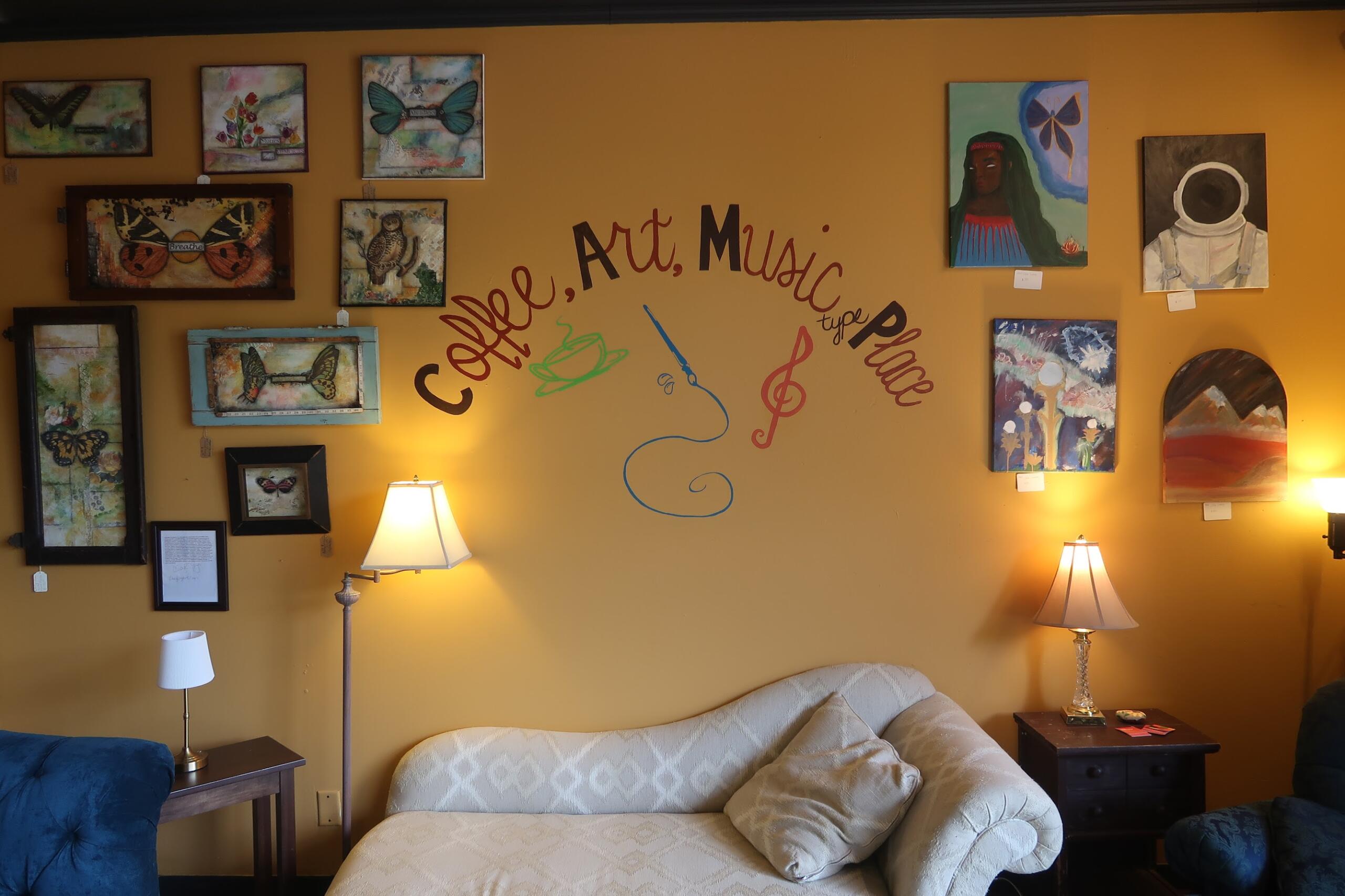 Living room with a gallery wall on a mustard-yellow wall, featuring many framed artworks around a cursive text design, a beige sofa, and two lamps.