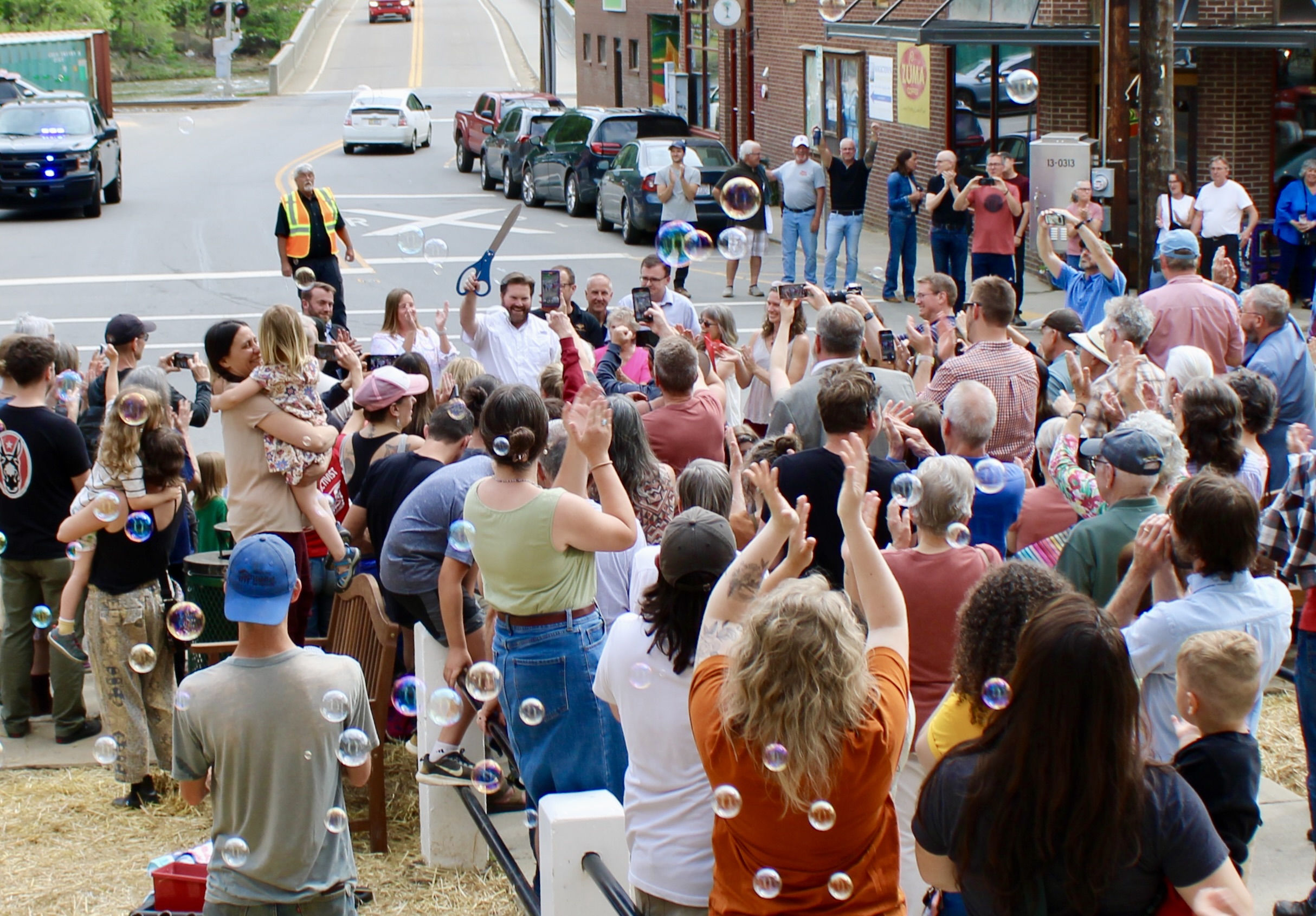 Crowd of people on a street festival, many taking photos as bubbles float through the air.
