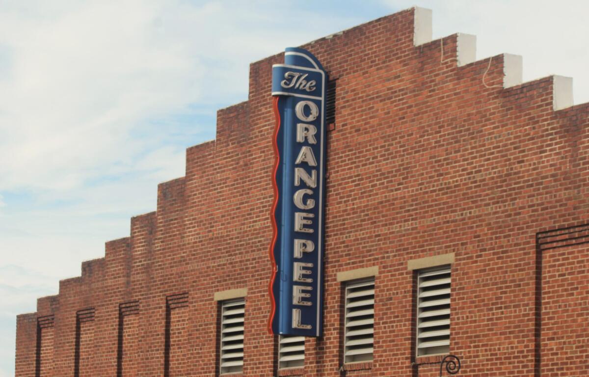 Brick building with a tall blue neon sign mounted along the corner, the sign featuring the word 'The' at the top and extending downward along the wall.