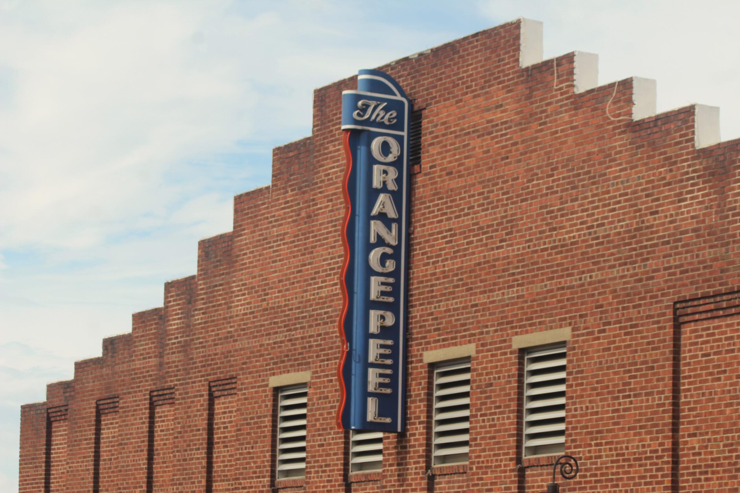 Brick building with a tall blue neon sign mounted along the corner, the sign featuring the word 'The' at the top and extending downward along the wall.