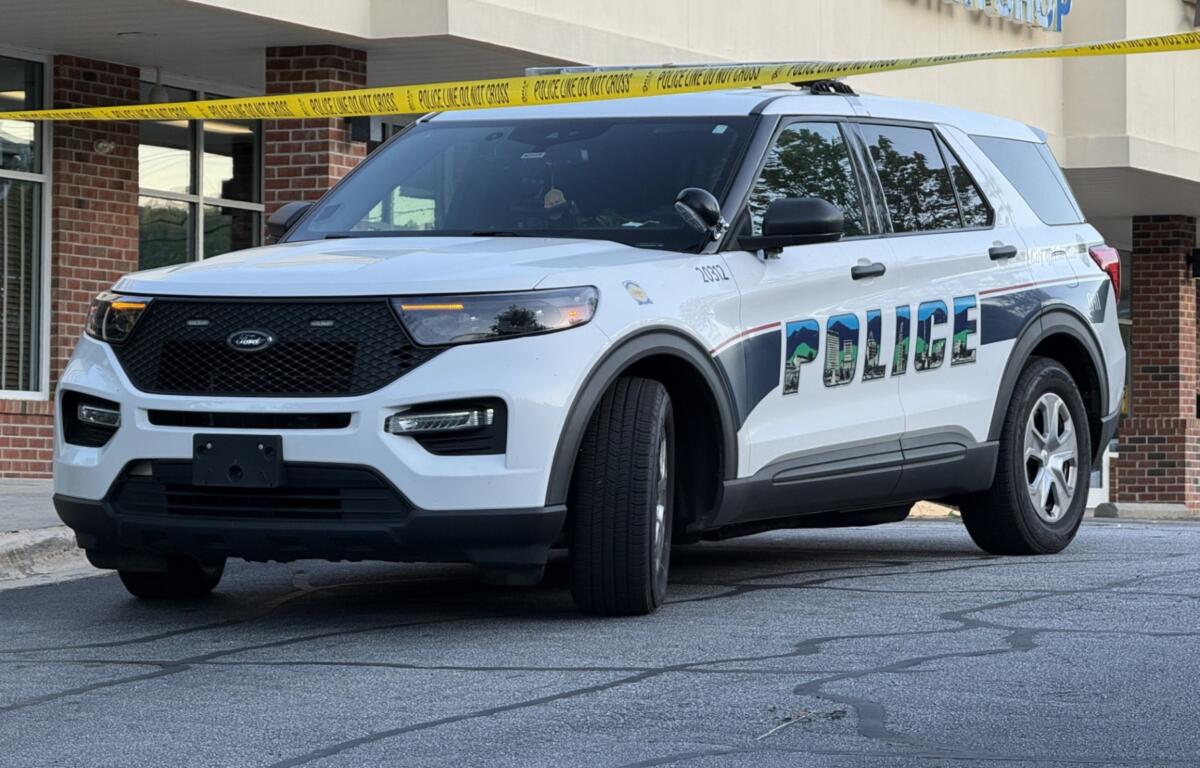 White Ford police SUV parked in front of a building with yellow police tape across the scene, 'POLICE' graphic on the side.