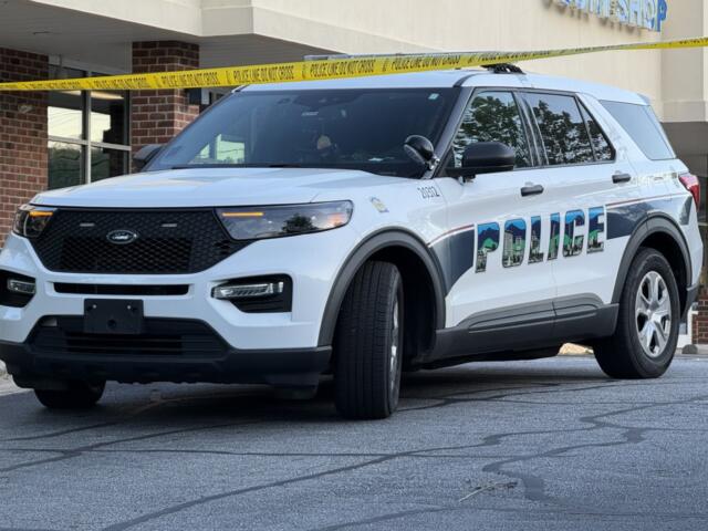 White Ford police SUV parked in front of a building with yellow police tape across the scene, 'POLICE' graphic on the side.
