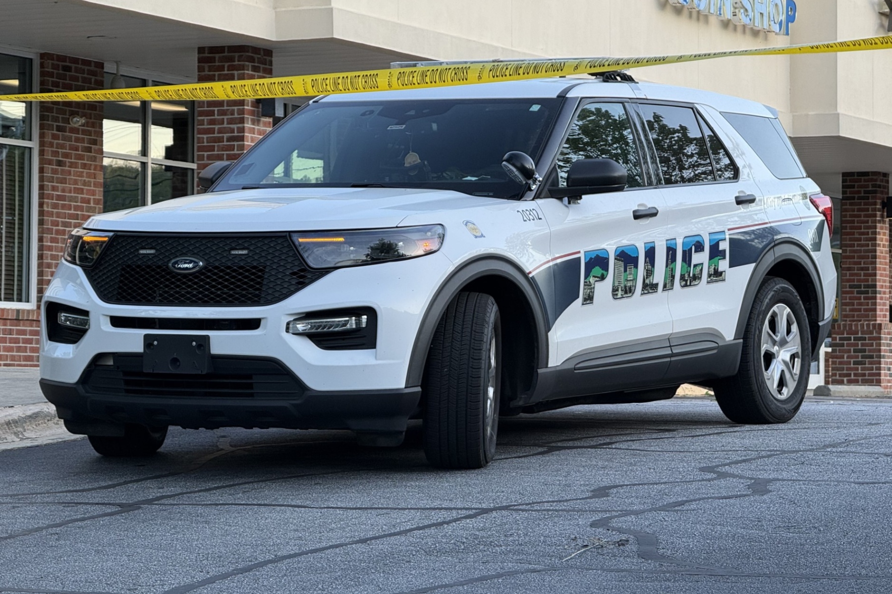 White Ford police SUV parked in front of a building with yellow police tape across the scene, 'POLICE' graphic on the side.