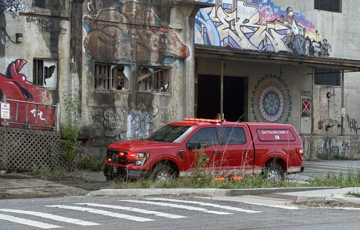 Red fire department utility vehicle parked in front of a graffiti-covered, dilapidated building with boarded windows and mural art
