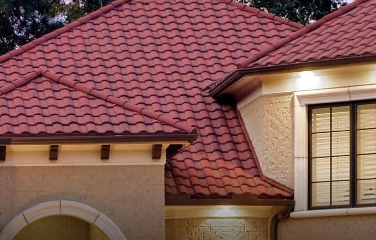 Red-tiled roof of a beige brick house, with a white arched entryway and large window with grid panes.