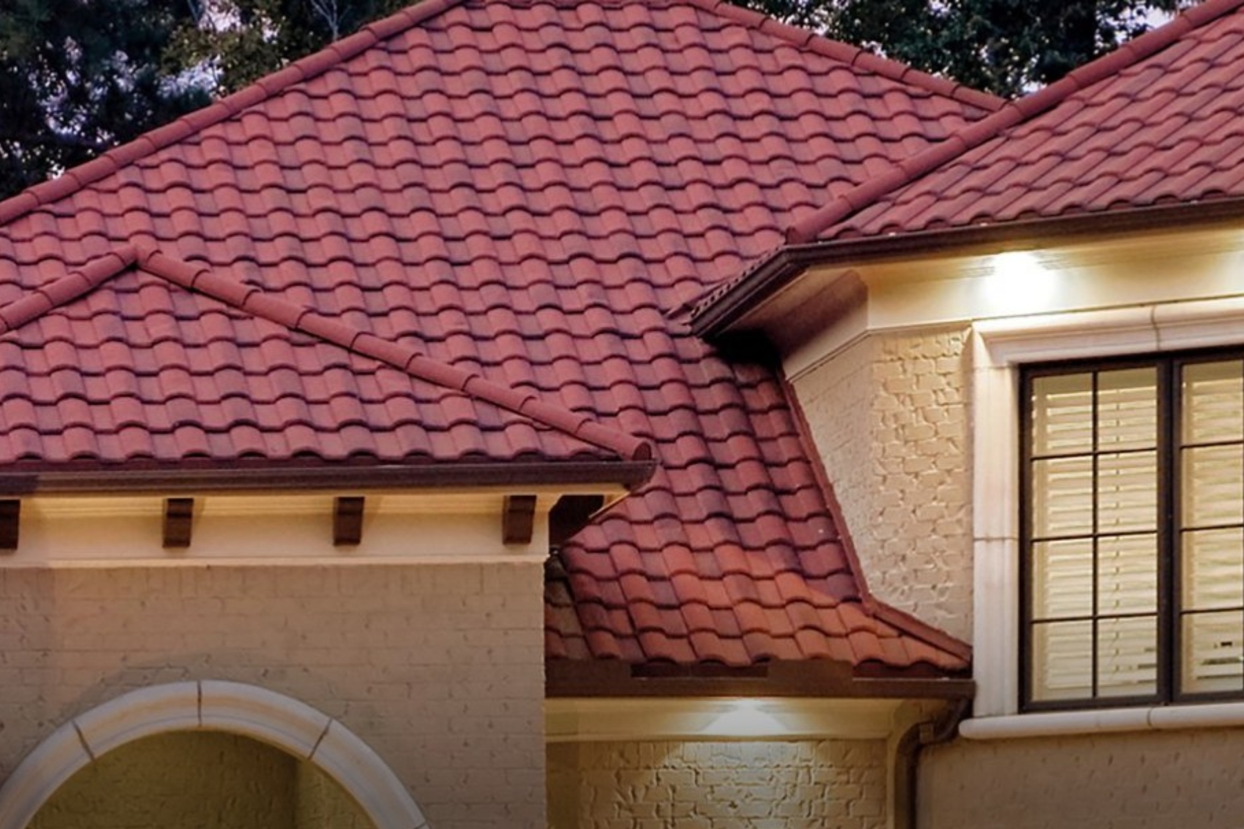 Red-tiled roof of a beige brick house, with a white arched entryway and large window with grid panes.