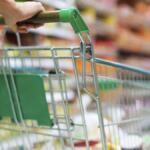 Shoppers push a shopping cart down a grocery store aisle with blurred shelves in the background.