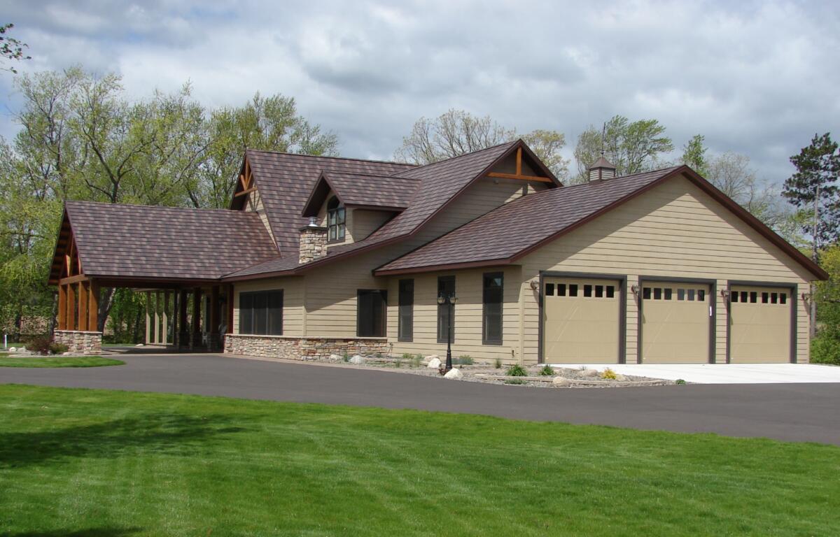 Beige two-story house with a three-car garage, brown shingle roof, and a neatly landscaped front yard.