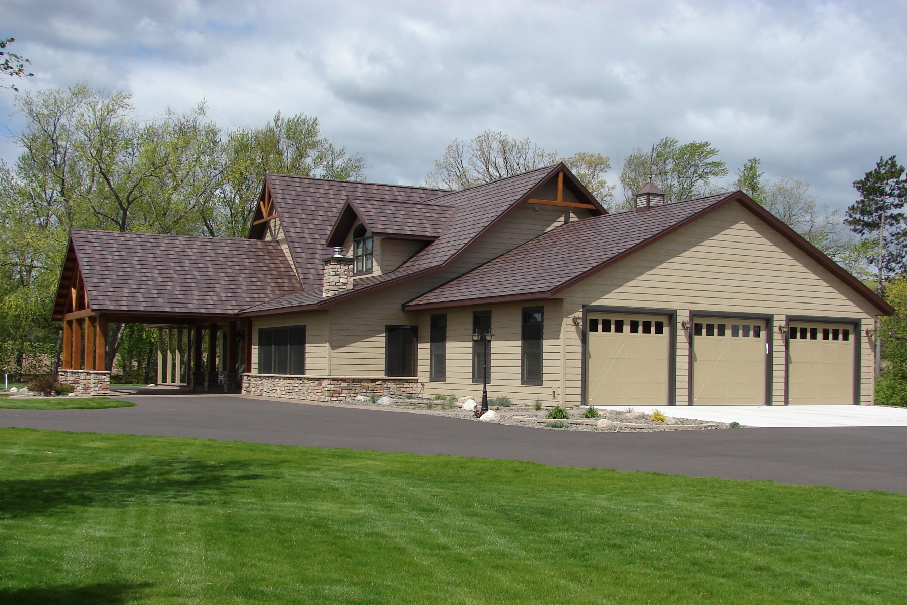 Beige two-story house with a three-car garage, brown shingle roof, and a neatly landscaped front yard.