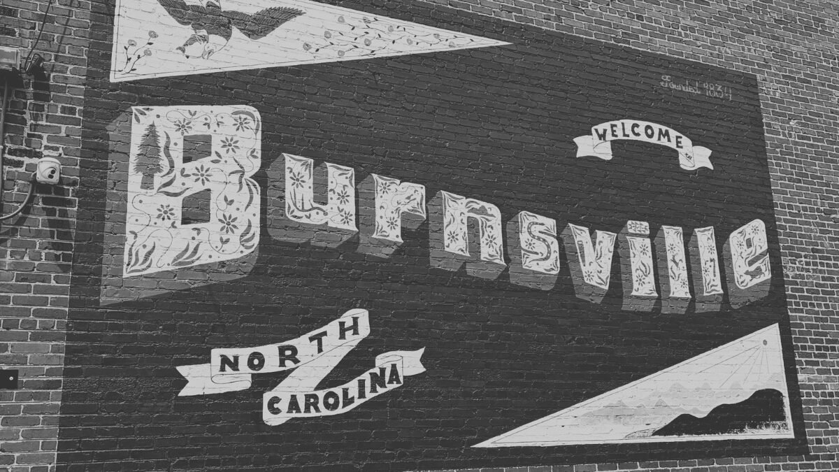 Brick-wall mural featuring ornamental text 'Burlington' with a 'Welcome' banner and ribbons reading 'North Carolina'—a city welcome sign.
