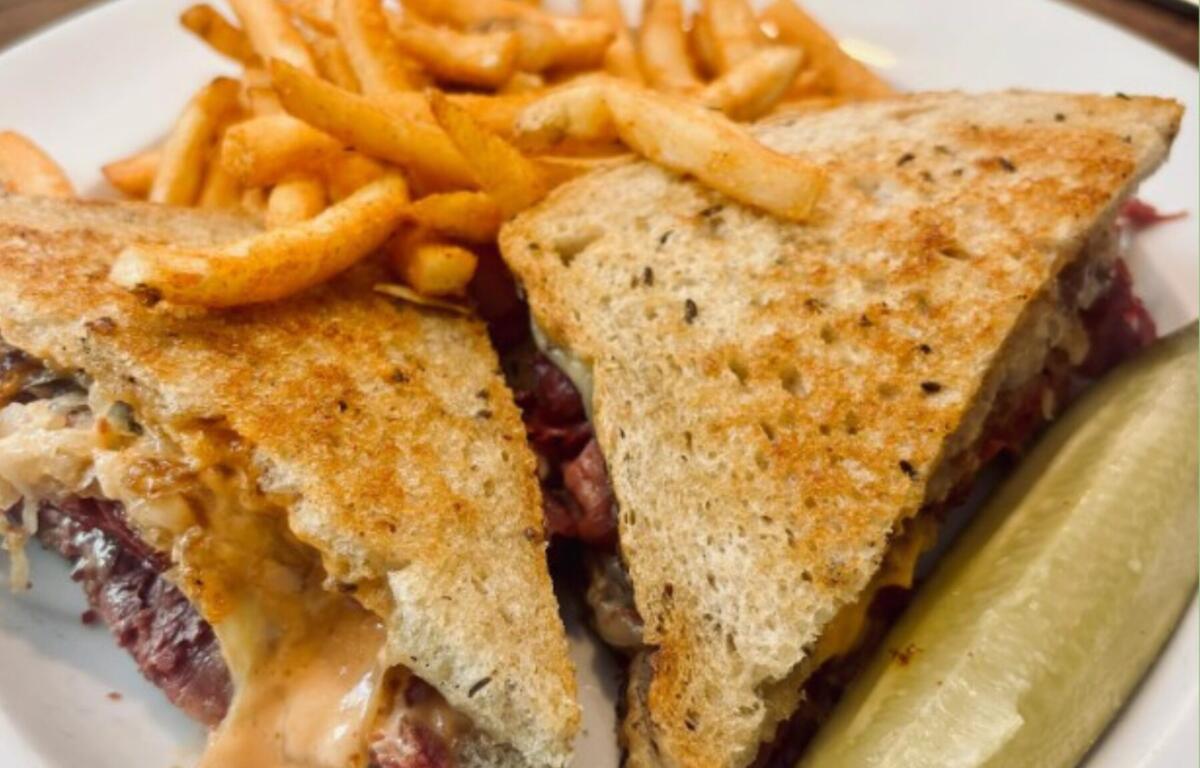 Grilled sandwich cut into triangles with melted cheese and meat, served with French fries and a pickle spear on a plate.