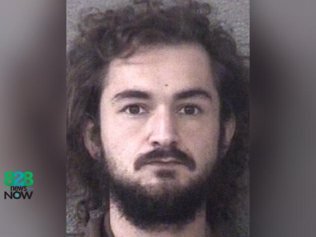 Mugshot-style head-and-shoulders photo of a man with long dark hair and a full beard, neutral backdrop, 828 News Now logo in the bottom left.
